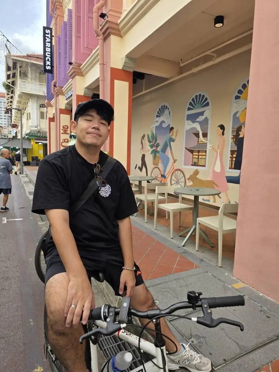 Kida cycling down a colorful street lined with shophouses