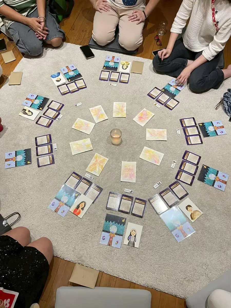 Overhead view of a group sitting around a circle of hand-illustrated cards laid out on a rug, with a candle lit in the middle