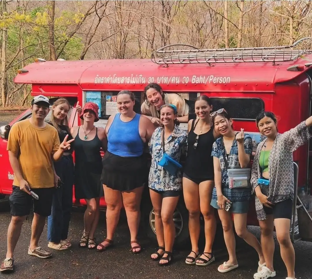 A group of friends posing by a red songthaew truck