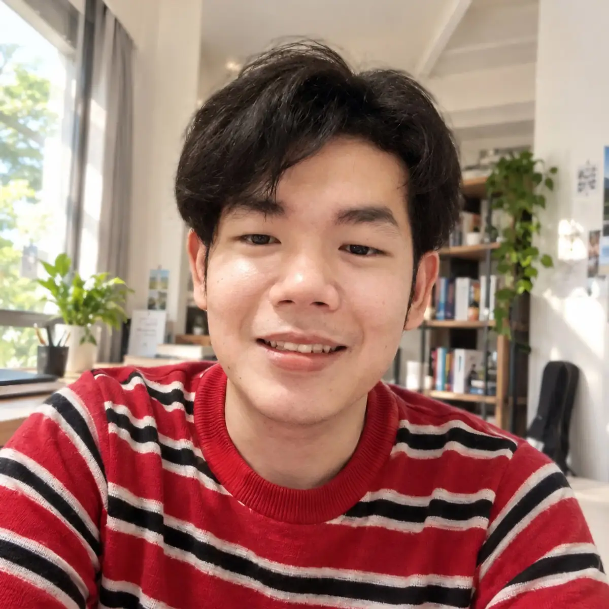 Kida smiling in a striped sweater, sitting in a bright room with plants and bookshelves