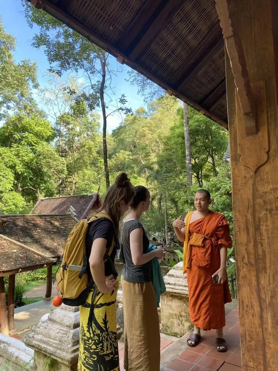 Kida and two guests pausing under a temple pavilion roof during the forest walk