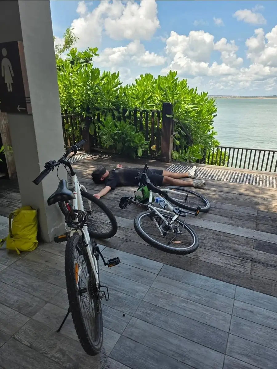 Kida lying flat on a wooden deck beside two bicycles, worn out after a full day of cycling around Singapore island